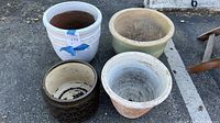 Four clay and ceramic pots arranged outdoors on asphalt, showing size and condition details.