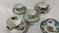 Overview of five fine bone china vintage teacups and saucers with floral and gilt detailing in various colors and patterns.