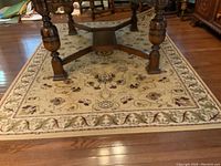 Full view of beige area rug with floral patterns under table on hardwood floor.