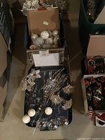 Christmas tree ornaments including silver glitter balls, pear-shaped baubles, crystal chandelier ornaments, decorative picks, displayed in and on plastic storage bins.
