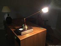 Photo of the desk lamp turned on, placed on top of Webster's Dictionary on a wooden desk.