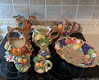 Eight colorful Fitz & Floyd ceramic pieces including pitchers, teapot, basket, and cream & sugar set with fruit and flower motifs.