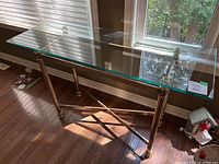 Front and top view of gold tone metal console table showing beveled glass top, light surface scratches, and gold-tone frame.