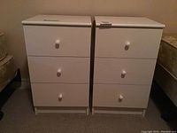 Front view of two identical white nightstands side by side, each with three drawers and round knobs.