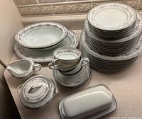 Noritake China dish set arranged on counter showing teacups, saucers, sugar bowl, butter dish, milk jug, and serving bowls.