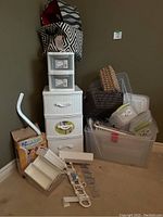Photo showing assortment of organizing storage items including plastic drawer units, fabric and wicker baskets, clear storage bins, hooks, drawer inserts, and EZ Moves furniture moving system.