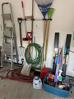 Full view of outdoor tools, ladders, hoses, and storage bin with assorted items