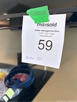 Close-up of the TV showing MaxSold auction lot number and Roku TV label taped on TV frame.