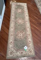 Full view of the sage green traditional runner rug laid on wooden floor showing its length and ornamental medallion patterns