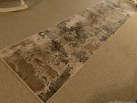 Full view of viscous runner rug laid flat on carpet, showing abstract pattern in neutral tones.