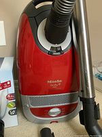 Red Miele Cat & Dog 5000 canister unit with attached flexible hose and stainless steel wand; box of vacuum bags visible at left