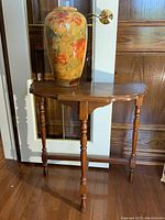 Full view of large ceramic vase placed on the mahogany demi lune table in front of a door, showing vase height and table style.