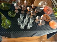Full view of assorted glassware on black cloth, showing pink depression glass coupe glasses, clear etched glasses, crystal parfaits, and colored glass bowls and plates.