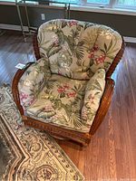 Front three-quarter view showing woven bamboo & rattan frame, curved armrests, and tropical print cushions.