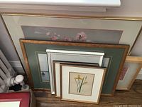 Photo showing six framed art prints stacked against a wall, various sizes and mats visible.