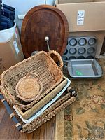 Photo of various wicker baskets stacked with wooden board and metal bakeware pans visible in background