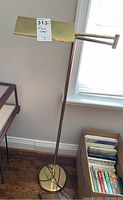 Full view of brass-colored floor lamp with round base and adjustable arm, labelled with lot number.
