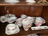 Bone china cups, small plates, and Hammersley trinket holder shown on wooden shelf.