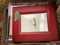 Stack of multiple photo frames in various materials including wood, composite, and metal, with a red wooden or composite frame on top.