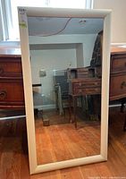 Full view of the large rectangular wall mirror with painted white wood frame on floor against a dresser. Visible scratches on frame.