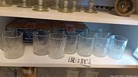 Two sets of six clear textured glasses displayed on a shelf with two original Oberglas boxes behind them.