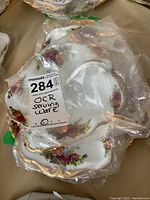 Six Old Country Roses porcelain serving dishes in clear plastic bags, showing floral pattern and gold trim.