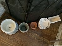 Seven plant cache pots arranged on floor, various sizes and materials visible