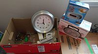 Box containing assorted small electronic accessories and Umbra wall clock.