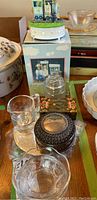 Photo shows the overall grouping of table accessories including a box music box, round metal jewelry box, glass candy bowls, and glass creamer and sugar bowl on top of metal trivets.