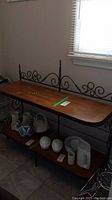 Photo showing whole wood console table with metal trim and decorative scrollwork, holding ceramic kitchenware on lower shelf
