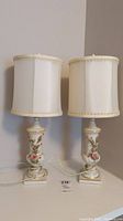 Pair of vintage ceramic floral table lamps with white fabric shades shown from front, indicating condition of shades