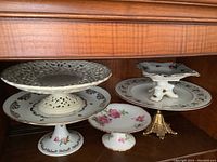 View of five footed serving plates showing detail and variety of design including pierced pattern, floral decoration, and gilded accents.