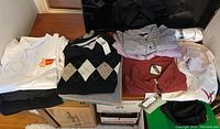 Various mens tops including sweaters, dress shirts, polo shirts, sweatshirt and windbreaker arranged on a table