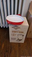 Dansk metal pot with red exterior and white interior placed on West Bend packaging box