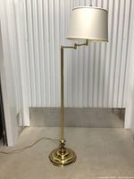 Full view of the brass floor lamp showing the base, vertical pole, swing arm, and white fabric shade.
