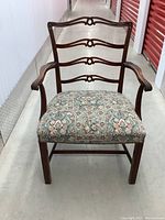 Front view of wooden ladder back arm chair with cushioned floral patterned seat, showing detail of three ladder back slats with circular accents.