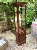 Full side view of a tall wood curio cabinet with three glass panels, wooden base, and glass shelves inside.