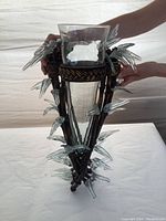 Front view of the glass and metal wall mounted vase with decorative glass finials held by hands to show scale and details.