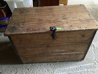 Front view showing wood planks on trunk top and front, iron latch and handles visible.