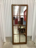 Large rectangular wooden frame mirror standing against a corrugated metal wall showing its height and divided panes