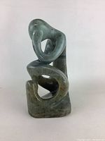 Front view of the green and brown solid stone abstract sculpture showing curved shapes forming a seated human figure.