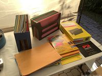 Photo of two plastic file holders filled with various colored hanging file folders, a yellow pack of Avery hanging file folders, and various file folders and envelopes on a table.