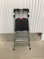 Front view of folding step ladder standing open showing two wide black plastic steps and silver side rails with black rubber tips on legs.