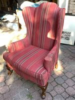 Front and side view of wingback chair showing overall shape, fabric pattern, and wood legs on paved surface.