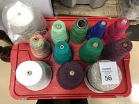 Photo of 12 cones of yarn in various colors, some labeled Forsell Savva and Spindlecraft. The yarn cones are arranged on a red surface.