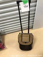 Closed view of tan and black insulated cooler bag with telescoping handle extended and wheels visible.