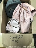 Photo of three backpacks and bags inside cardboard box showing large beige backpack, small light pink backpack, and black backpack