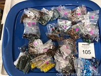 Multiple small plastic bags containing assorted beads in various colors and types arranged on a blue plastic lid with a lot number card.