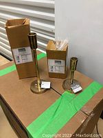Two brass antique candlestick holders side by side with original packaging boxes behind them.