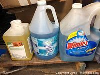 Three large plastic jugs of cleaning liquid, two are glass cleaners and one a general cleaner